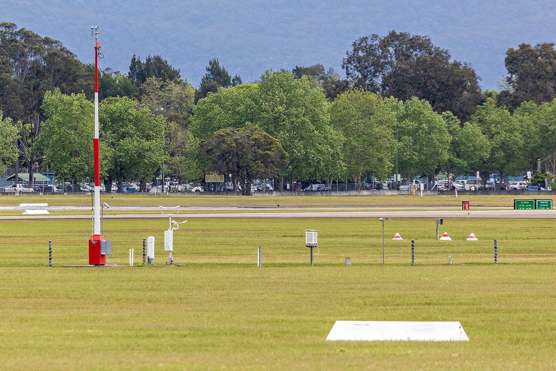 An automatic weather station — instrument mast and rain gauge — in an open field
